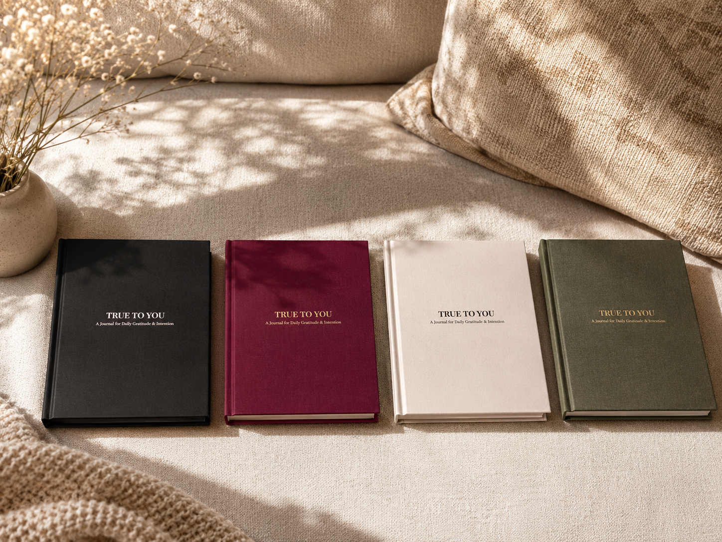 Four True To You journals in dark chocolate, bordeaux, ivory and olive laid out on cream linen